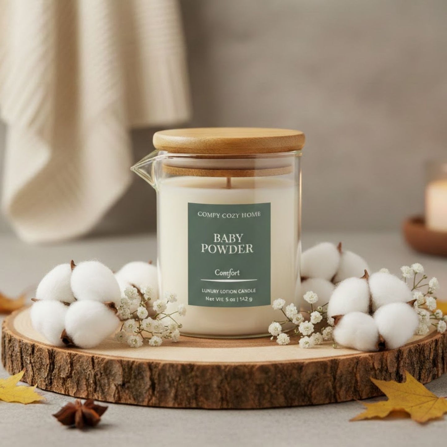 Candle labeled 'Baby Powder' on a wooden coaster with cotton and leaves.