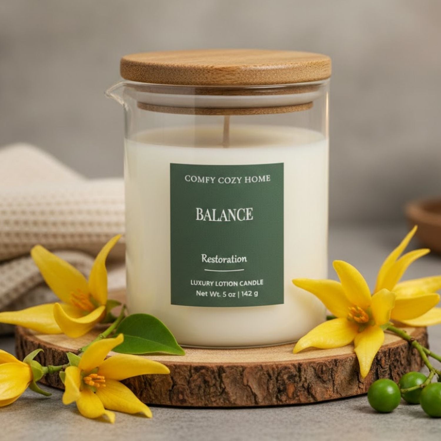 Candle labeled 'Balance' from 'Comfy Cozy Home' with wooden lid and yellow flowers around on a wooden coaster.